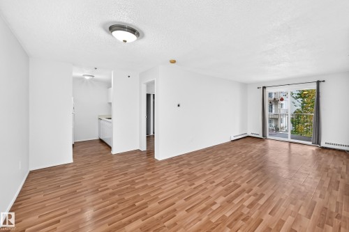 Open layout living area with wood-finish flooring, white walls, and a sliding glass door to a balcony - #212 11218 80 St Nw, Edmonton, AB 
