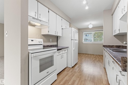 Kitchen featuring white cabinetry, wood-finish flooring, dual-basin stainless steel sink, and white appliances - 55 Royal Road Nw, Edmonton, AB 