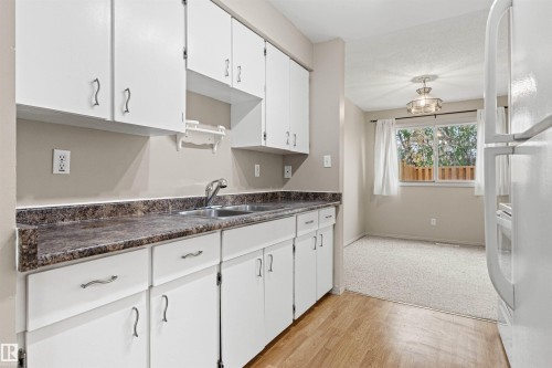 Kitchen featuring white cabinetry, dark stone-finish countertops, stainless steel dual-basin sink, and wood-finish flooring - 55 Royal Road Nw, Edmonton, AB 