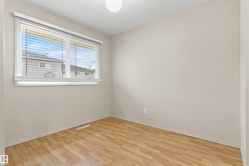 Neutral-toned interior featuring wood-finish flooring and a single-hung window with adjustable horizontal blinds - 55 Royal Road Nw, Edmonton, AB 