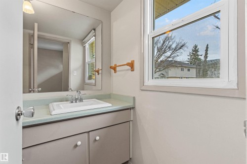 Built-in vanity featuring a solid-surface countertop, rectangular drop-in sink, chrome faucet, wall-mounted mirror, and natural light via a dual-pane window - 55 Royal Road Nw, Edmonton, AB 