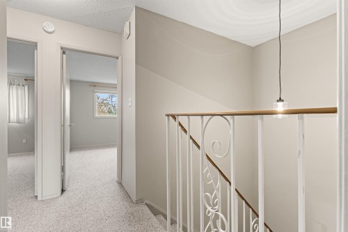 White metal stair railing with decorative scrollwork, wooden handrail, and a single pendant light fixture - 55 Royal Road Nw, Edmonton, AB 