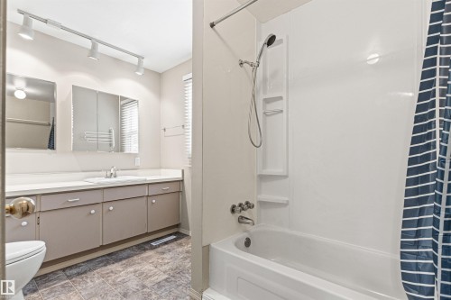 Bathroom featuring a tub-shower combination with integrated shelving, vanity with a solid-surface countertop, mirrored medicine cabinet, and track lighting - 55 Royal Road Nw, Edmonton, AB 