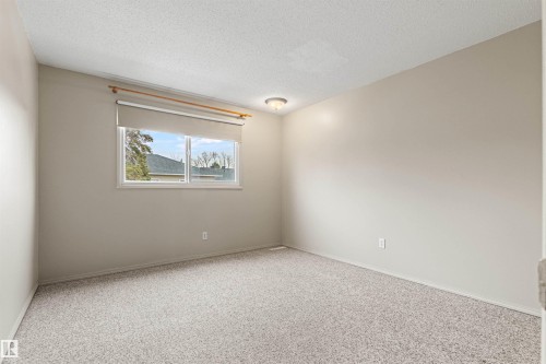 Neutral-toned room featuring carpeted flooring, textured ceiling, flush-mount lighting, and a single-pane horizontal window with a retractable shade - 55 Royal Road Nw, Edmonton, AB 