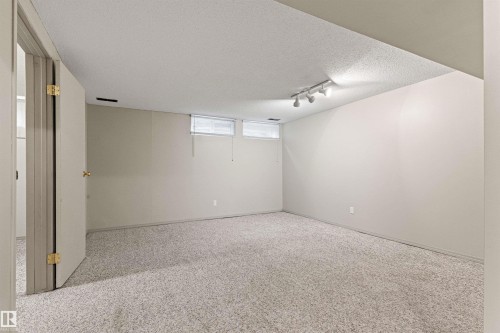 Neutral-toned room featuring wall-to-wall carpeting, recessed ceiling lighting, two horizontal windows, and a hinged interior door - 55 Royal Road Nw, Edmonton, AB 