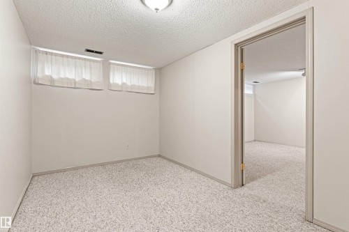 Neutral-toned interior room featuring wall-to-wall carpeting, two rectangular above-grade windows, and a doorway with a neutral-finish door frame - 55 Royal Road Nw, Edmonton, AB 