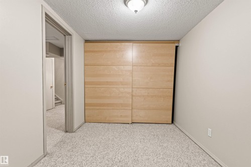 Room featuring neutral wall tones, carpeted flooring, and large sliding closet doors with a light wood finish - 55 Royal Road Nw, Edmonton, AB 