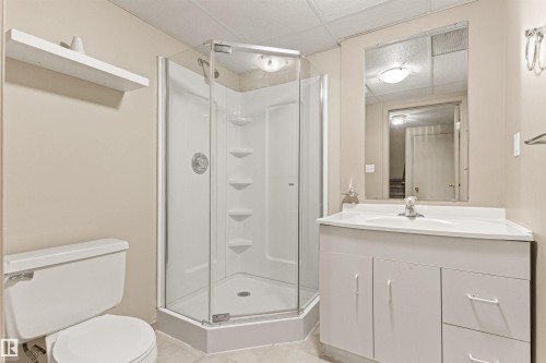 Corner shower stall with glass enclosure and integrated shelving, white vanity cabinet featuring an integrated sink, wall-mounted storage shelf, and recessed ceiling lighting - 55 Royal Road Nw, Edmonton, AB 