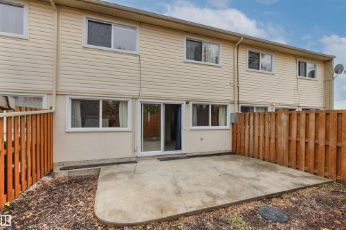Exterior rear elevation featuring beige horizontal siding, a concrete patio, and a wood privacy fence - 55 Royal Road Nw, Edmonton, AB 