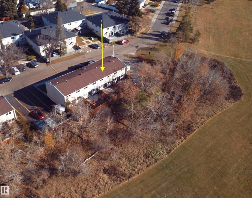 Aerial perspective of multi-unit building featuring a gabled shingle roof, paved parking area, and wood decking, bordered by expansive open green space and mature trees - 55 Royal Road Nw, Edmonton, AB 