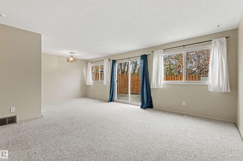 Neutral-toned living space featuring wall-to-wall carpeting, large windows, sliding glass door, and a multi-arm ceiling-mounted light fixture - 55 Royal Road Nw, Edmonton, AB 