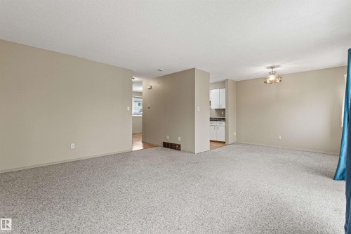 Neutral-toned interior space featuring wall-to-wall carpeting, a multi-bulb flush-mount light fixture, and white built-in kitchen cabinetry - 55 Royal Road Nw, Edmonton, AB 