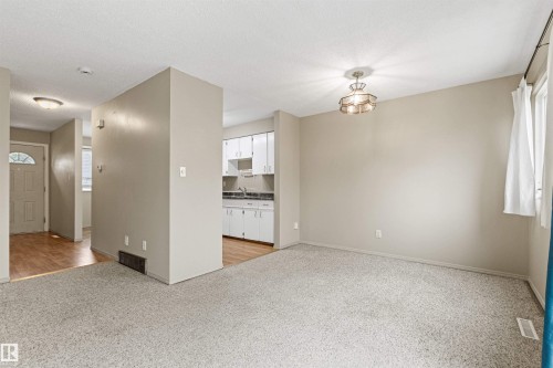 Neutral wall-to-wall carpeting, wood-finish flooring, white cabinetry, and multi-tier pendant lighting - 55 Royal Road Nw, Edmonton, AB 