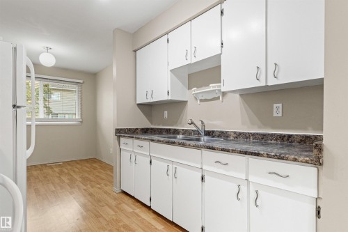 Kitchen featuring white cabinetry, stone-pattern laminate countertops, a stainless steel dual-basin sink, and wood-finish flooring - 55 Royal Road Nw, Edmonton, AB 