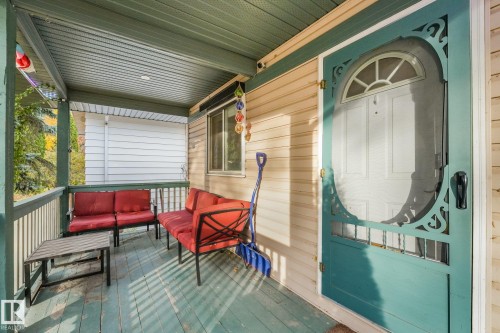 Covered front porch featuring horizontal vinyl siding, a painted wood-slat floor, a decorative arched screen door, and a beadboard ceiling - 9617 151 Street Nw, Edmonton, AB 
