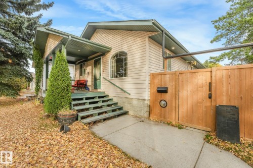 Single-story residence featuring light-toned horizontal siding, a covered entryway with painted wood steps, an arched window, and a wood privacy fence - 9617 151 Street Nw, Edmonton, AB 