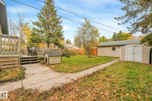Backyard featuring a raised wooden deck, detached garage, storage shed, and concrete walkway - 9617 151 Street Nw, Edmonton, AB 