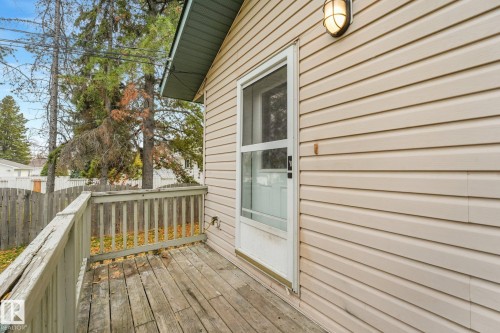 Exterior deck featuring wood-plank flooring, horizontal vinyl siding, a glass-panel storm door, and an attached wall-mounted sconce - 9617 151 Street Nw, Edmonton, AB 