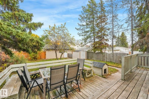 Elevated wood deck featuring integrated bench seating and perimeter railing, overlooking a fenced backyard with mature trees and a detached storage shed - 9617 151 Street Nw, Edmonton, AB 