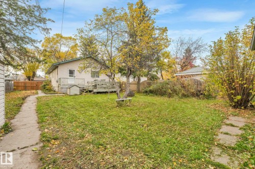 Rear exterior featuring a wood deck, concrete walkways, wood privacy fencing, and mature trees - 9617 151 Street Nw, Edmonton, AB 