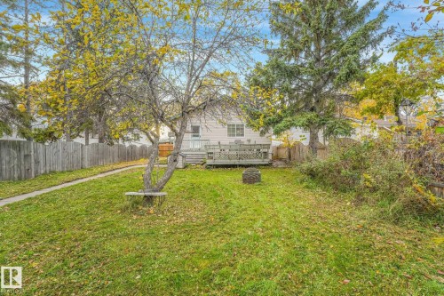 Rear yard featuring a wood deck, perimeter wood fencing, concrete pathway, and mature trees - 9617 151 Street Nw, Edmonton, AB 