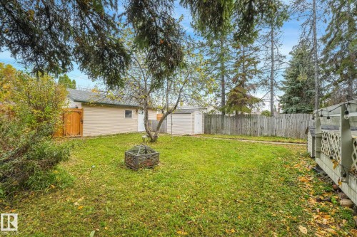 Backyard featuring a grass lawn, perimeter wood fencing, detached storage structure, and elevated deck with lattice detailing - 9617 151 Street Nw, Edmonton, AB 