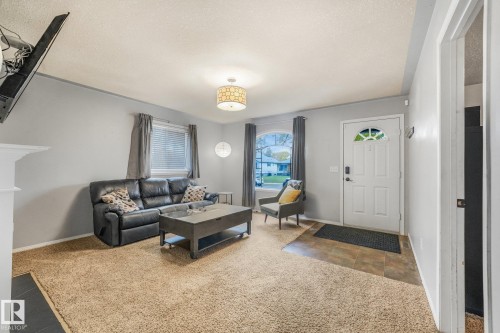 Living area featuring neutral wall paint, carpeting, an arched window, a tiled entryway, and a semi-flush mount drum light fixture - 9617 151 Street Nw, Edmonton, AB 