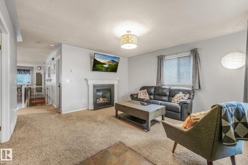 Living space featuring a fireplace with a decorative mantel, neutral carpet flooring, a multi-pane window, and drum-style overhead lighting - 9617 151 Street Nw, Edmonton, AB 