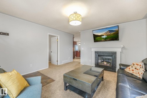 Living area featuring a fireplace with a dark stone-finish surround, a white mantel, and a decorative drum-style ceiling light fixture - 9617 151 Street Nw, Edmonton, AB 