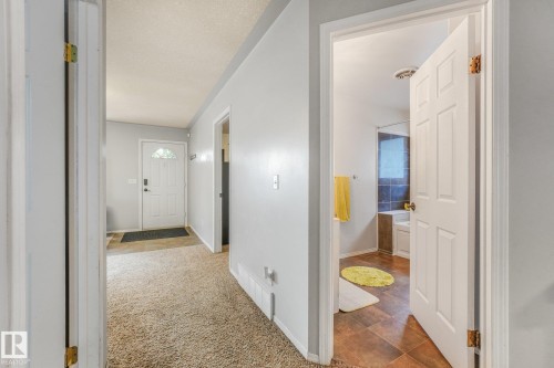 Interior corridor featuring neutral wall finishes, carpeted flooring, and a six-panel entry door with transom window - 9617 151 Street Nw, Edmonton, AB 
