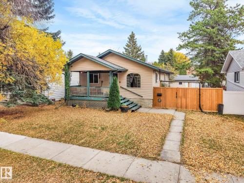 Exterior featuring horizontal siding, a covered front porch with railing, an arched window, and a wood privacy fence - 9617 151 Street Nw, Edmonton, AB 