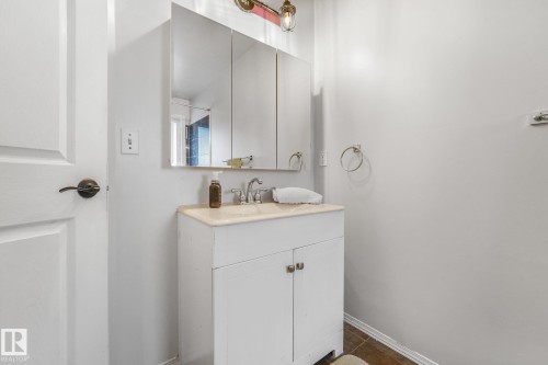 Vanity featuring a white cabinet, countertop with an integrated sink, tri-panel mirrored medicine cabinet, and wall-mounted light fixture - 9617 151 Street Nw, Edmonton, AB 