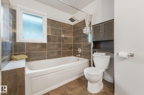 Full-size bathtub with surrounding wall tile, built-in storage cabinet, window with frosted glass, and tile flooring - 9617 151 Street Nw, Edmonton, AB 