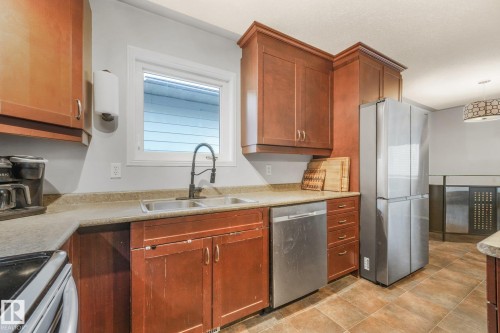 Kitchen featuring wood cabinetry, stainless steel appliances, dual-basin sink with matte black faucet, and ceramic tile flooring - 9617 151 Street Nw, Edmonton, AB 