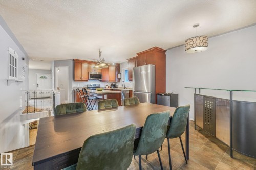 Kitchen featuring wood cabinetry, an island with stone-finish countertops, stainless steel appliances, tile flooring, and a decorative drum pendant light - 9617 151 Street Nw, Edmonton, AB 