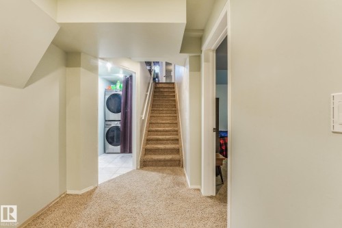 Carpeted staircase with white handrail, recessed laundry area featuring tile flooring, and neutral wall paint - 9617 151 Street Nw, Edmonton, AB 