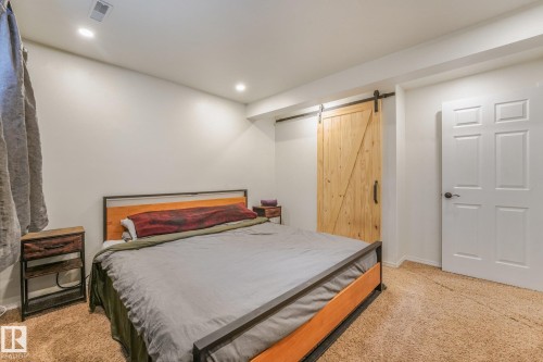 Room featuring neutral wall tones, recessed lighting, carpeted flooring, a light wood-finish sliding barn door, and a standard six-panel door - 9617 151 Street Nw, Edmonton, AB 