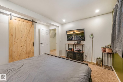Natural wood-finish sliding barn door with black iron hardware, recessed lighting, and wall-mounted television bracket - 9617 151 Street Nw, Edmonton, AB 