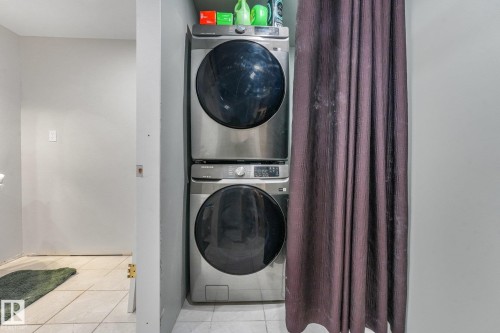 Stacked, front-loading stainless steel laundry appliances set within a recessed alcove featuring tile flooring - 9617 151 Street Nw, Edmonton, AB 