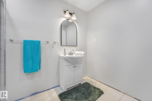 White vanity with a pedestal-style sink, arched wall mirror, two-light fixture, and light-toned tile flooring - 9617 151 Street Nw, Edmonton, AB 