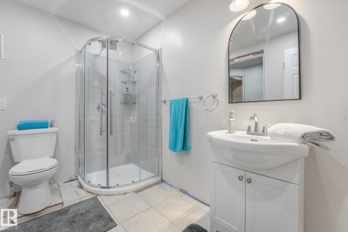Bathroom featuring a glass-enclosed corner shower with tile surround, white vanity cabinet with a integrated basin, chrome plumbing fixtures, and an arched wall mirror - 9617 151 Street Nw, Edmonton, AB 