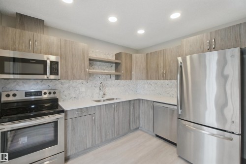 Kitchen featuring stainless steel appliances, wood-finish cabinetry, light countertops, and a herringbone-patterned backsplash - 13212 73 Street Nw, Edmonton, AB 