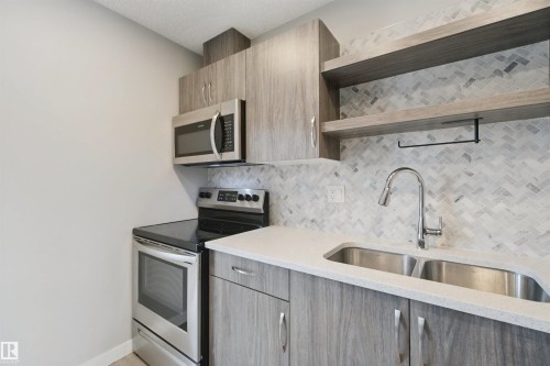Stainless steel appliances, herringbone tile backsplash, light wood-finish cabinetry, light-toned countertop, and a dual basin stainless steel sink - 13212 73 Street Nw, Edmonton, AB 