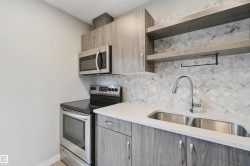 Stainless steel appliances, herringbone tile backsplash, light wood-finish cabinetry, light-toned countertop, and a dual basin stainless steel sink - 