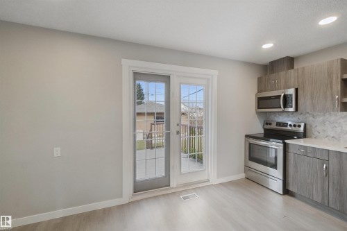Kitchen featuring wood-finish cabinetry, stainless steel appliances, a patterned tile backsplash, recessed lighting, and patio doors - 13212 73 Street Nw, Edmonton, AB 