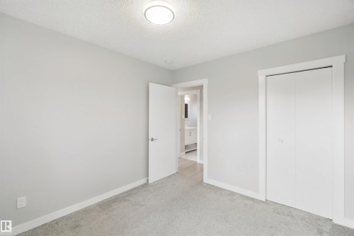 Soft grey carpeting, neutral wall color, contemporary flush-mount ceiling light, white bi-fold closet doors, and white interior door with polished chrome hardware - 13212 73 Street Nw, Edmonton, AB 