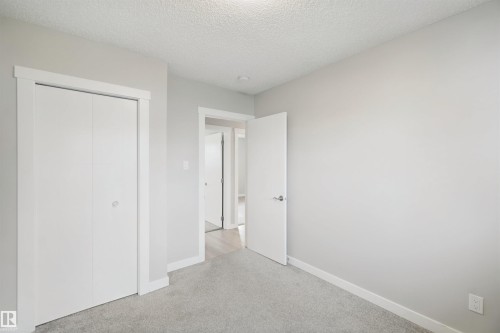 Wall-to-wall carpeting in a neutral tone, white bi-fold closet doors with white trim, and a white interior door - 13212 73 Street Nw, Edmonton, AB 