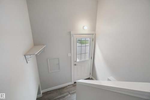 Entryway featuring a white paneled door with glass inserts, wood-finish flooring, a wall-mounted light fixture, and a built-in shelving unit with hooks - 13212 73 Street Nw, Edmonton, AB 
