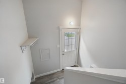 Entryway featuring a white paneled door with glass inserts, wood-finish flooring, a wall-mounted light fixture, and a built-in shelving unit with hooks - 