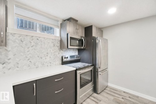 Kitchen featuring a herringbone tile backsplash, white countertops, wood-finish flooring, and stainless steel appliances - 13212 73 Street Nw, Edmonton, AB 